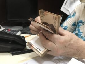 mano contando billetes mexicanos sobre escritorio