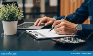 persona firmando documentos con calculadora y laptop